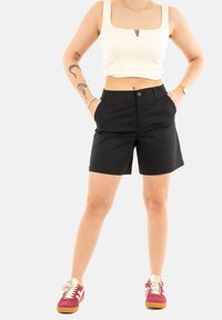 Pantaloni corti neri con tasche laterali, realizzati in un materiale leggero. Abbinati a un top corto bianco con scollatura quadrata. Scarpe da ginnastica rosse.