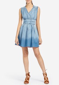 Sukienka dżinsowa, jasnoniebieska, z fasonem kopertowym, bez rękawów, dopasowana góra, marszczona talia, plisowany dół i postrzępiony brzeg. Akcentowana brązowymi sandałami na paski.