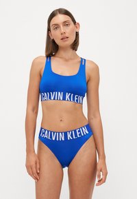 Blauwe bikini set gemaakt van soepel materiaal. Beha heeft een brede CALVIN KLEIN band. Hoge taille slipjes met een vergelijkbaar band ontwerp.