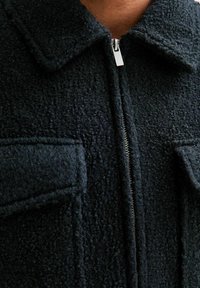 Czarna teksturowana kurtka z puszystą powierzchnią, zapięciem na zamek i kołnierzem. Posiada dwie przednie kieszenie z klapami dla dodatkowego akcentu.