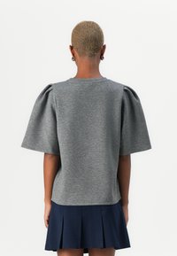 Top grigio a maniche corte con scollatura rotonda e maniche a sbuffo arricciate, realizzato in tessuto morbido, abbinato a una gonna navy plissettata.