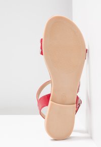 Sandale rouge avec semelle texturée beige et talon carré, affichant la taille 37 estampillée sur la semelle, positionnée contre un fond blanc d'angle.