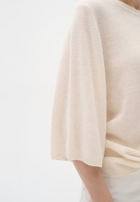 Suéter de punto beige claro con un corte relajado y mangas anchas. Tejido texturizado con puños y escote acanalados. Diseño minimalista, sin patrones.