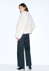 Jachetă albă din blană sintetică, cu decolteu rotund, mâneci lungi și textură pufoasă. Asortată cu pantaloni negri, cu talie înaltă, prevăzuți cu ținte argintii.