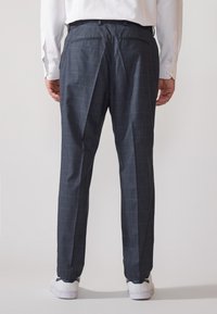Pantaloni a quadri grigio scuro con vestibilità su misura, dotati di tasche posteriori e una texture in tessuto liscia. Abbinati a sneakers bianche.