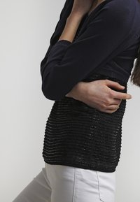 Svart texturerad topp med horisontella linjer, korta ärmar och rundad halsringning, i kombination med vita byxor.