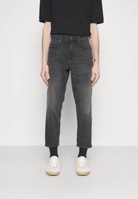 Jeans in denim grigio con una vestibilità regolare, lunghezza cropped e leggera sbiaditura. Abbinati a sneakers bianche e calzini neri alla caviglia.