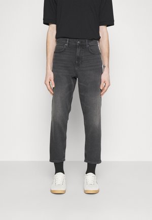 Jeans de mezclilla gris con una fit regular, largo recortado y un desvanecimiento sutil. Combinados con zapatillas blancas y calcetines negros de caña baja.