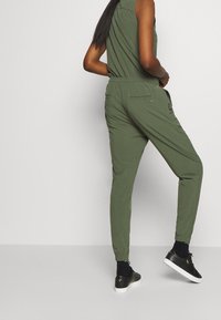 Zelené tepláky s elastickým pasem, zúženými nohavicemi a bočními kapsami. V kombinaci s černými teniskami. Hladká, lehká látka.