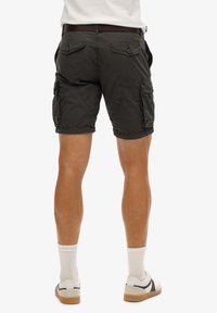 Grijze cargoshorts met zakken en stikdetails, gecombineerd met witte sokken en sneakers. Achteraanzicht dat de beenvorm benadrukt.