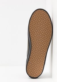Semelle d'une chaussure avec un motif en caoutchouc texturé de couleur marron, bordée d'un matériau noir. Présente un design géométrique clair pour une meilleure adhérence.