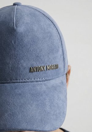Blauwe suède honkbalpet met gestikte panelen en metalen logo "ANTONY MORATO" aan de voorkant, gedragen door een persoon met een lichte huidtint.