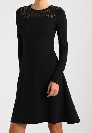 Vestido negro de manga larga con un corsé ajustado y una falda acampanada, que presenta un panel de encaje transparente en el escote con un sutil patrón de leopardo.