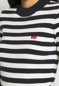 Pull rayé noir et blanc avec texture côtelée. Présente un col rond et un petit logo rouge Levi's à l'avant.