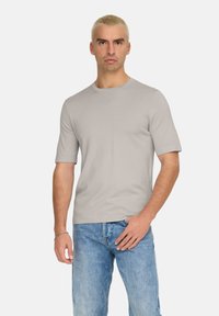 T-shirt grigio chiaro a maniche corte con scollatura a giro, realizzata in un tessuto liscio. Design semplice senza loghi o motivi visibili.