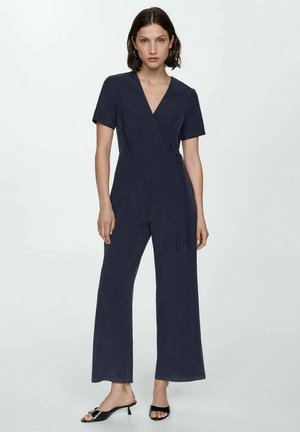 Mörkblå omlottdress med korta ärmar, vida ben och ett tygband i midjan. Slät struktur, minimalistisk design.