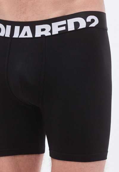Črne boksarske kratke hlače iz gladkega blaga, z širokim belim elastičnim pasom, na katerem je jasno prikazan logotip "SQUARED2".