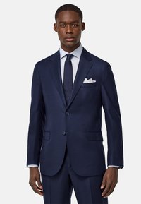 Costume bleu marine avec un revers cranté, deux boutons et des poches avant. Comprend un mouchoir de poche blanc et une cravate sombre assortie. Texture lisse.