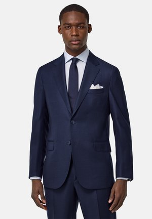 Navy blue suit with a notched lapel, two buttons, and front pockets. Features a white pocket square and matching dark tie. Smooth texture.