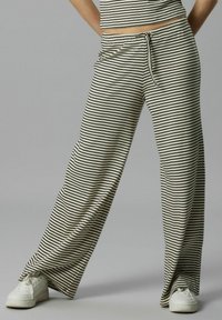 Pantalons larges rayés en tissu beige et noir, avec une taille élastique à cordon de serrage et une coupe décontractée, associés à des baskets blanches.