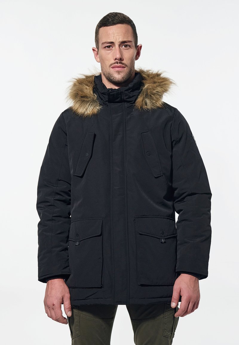 Parka nera con cappuccio foderato in pelliccia, dotata di due tasche frontali e chiusura con zip, realizzata in un tessuto resistente.