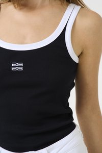 Canottiera nera a coste con profili bianchi. Presenta un logo al centro. Tessuto testurizzato, design aderente, indossata con pantaloni bianchi.