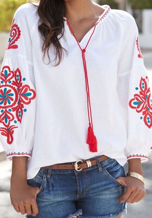Biała haftowana bluzka z długimi, szerokimi rękawami ozdobionymi czerwonymi i turkusowymi wzorami, dekoltem z wycięciem i czerwonym chwostem oraz dekoracyjną lamówką.