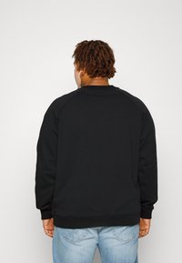 Black sweatshirt with raglan sleeves, textured fabric, and ribbed cuffs and hem, worn with light blue denim jeans.