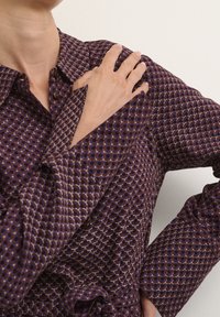 Bluzka z długim rękawem w ciemnofioletowym materiale z geometrycznym wzorem, posiadająca szpiczasty kołnierzyk i zapinana na guziki z przodu, miękka w dotyku, z detalami mankietów.