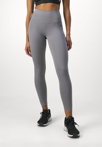 Leggings grigi con vita alta e tessuto lisciante. Presentano un pannello testurizzato in vita e una silhouette aderente. Calzature nere in abbinamento.