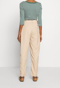 Randig gröna och vita långärmad topp, beige högmidjade byxor, och bruna slip-on skor. Slät tyg; avslappnad passform; bakfickor synliga.