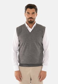 Gilet di lana grigia con scollatura a V, indossato sopra una camicia bianca con colletto. Il gilet ha una superficie liscia e una forma aderente.
