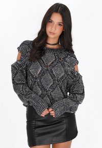 Gebreide trui met zwart-wit ruitpatroon, off-shoulder ontwerp en dikke manchetten, gecombineerd met een zwarte leren minirok.