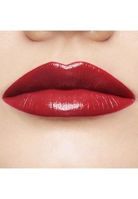 Rote Lippenstift auf glatten, vollen Lippen mit einem glänzenden Finish. Die Farbe ist lebhaft und tief, wodurch die Kurve der Lippen betont wird.