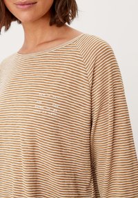 Langärmliges, leichtes Hemd in beige und weißen Streifen. Verfügt über einen subtilen Textdruck in Weiß auf der Vorderseite. Weiche Textur, entspannte Passform.