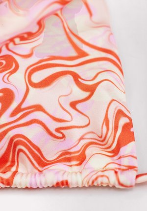 Tissu avec un motif abstrait ondulé rouge, rose et blanc, bord élastique froncé sur une surface lisse.