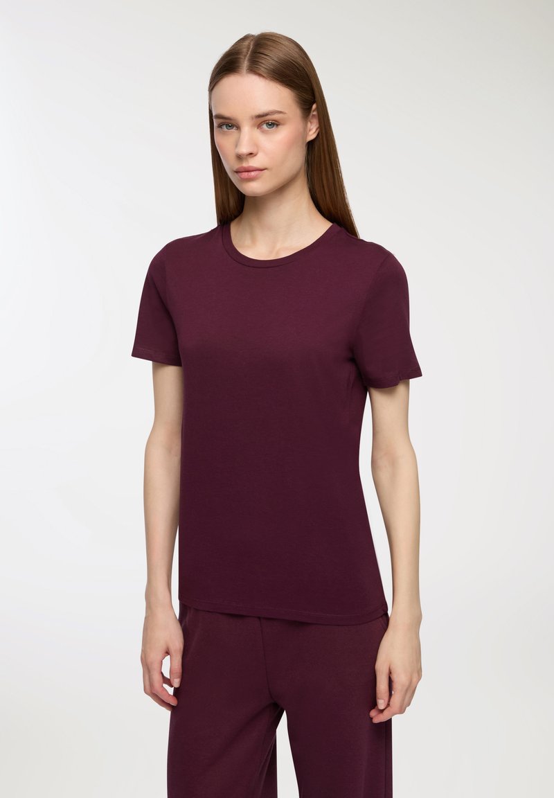 Bordowa koszulka z krótkim rękawem wykonana z miękkiego materiału, z okrągłym dekoltem i luźnym krojem, zestawiona z pasującymi spodniami.