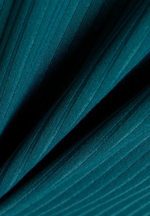 Tissu côtelé vert sarcelle foncé plié en diagonale, montrant la texture et des ombres subtiles créant de la profondeur.