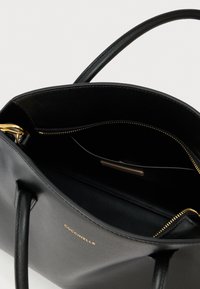 Zwarte leren handtas met gouden ritssluiting, merk "Coccinelle", met het open hoofdvak en handvatten zichtbaar tegen een witte achtergrond.