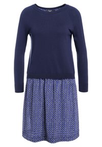 Robe bleu marine avec un haut en tricot et une jupe à motifs géométriques en blanc et bleu. Dotée de manches longues et d'une taille froncée.