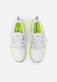 Witte sportieve schoenen met grijze accenten, felgele zool, stoffen bovenwerk, ronde neus en traditionele vetersluiting.