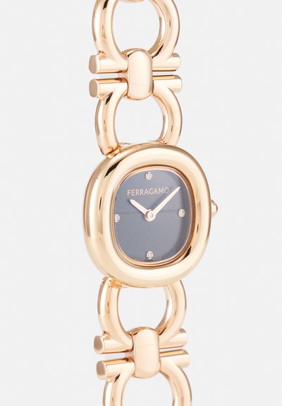 Gold-tone metal watch with a rounded face, dark dial, and diamond accents. Features linked chain design with polished finish.