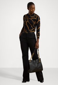 Tricou negru cu mâneci lungi și model de lanț auriu, pantaloni negri ajustați și o geantă de umăr neagră cu curea de lanț aurie și detalii cu logo.