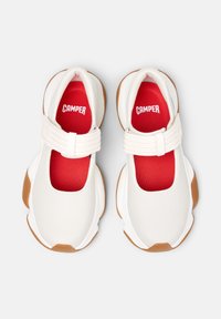 Zapatos blancos de tipo slip-on con plantillas rojas y una correa de velcro, que cuentan con una suela acolchada y un diseño redondeado, mostrados desde arriba.