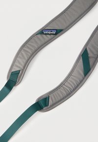 Γκρι επενδυμένοι ιμάντες σακιδίου με πράσινη ρυθμιζόμενη ζώνη από ίνες και ένα λογότυπο της μάρκας Patagonia σε έναν ιμάντα, πάνω σε λευκό φόντο.