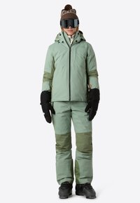 Giacca e pantaloni da snowboard verde menta con accenti verde scuro; presenta guanti neri e snowboot; design sportivo con tasche con zip.