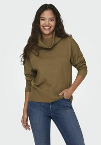 Pull à col montant vert olive avec des poignets et un ourlet côtelés, associé à un jean bleu foncé. Texture douce, coupe décontractée et manches longues.