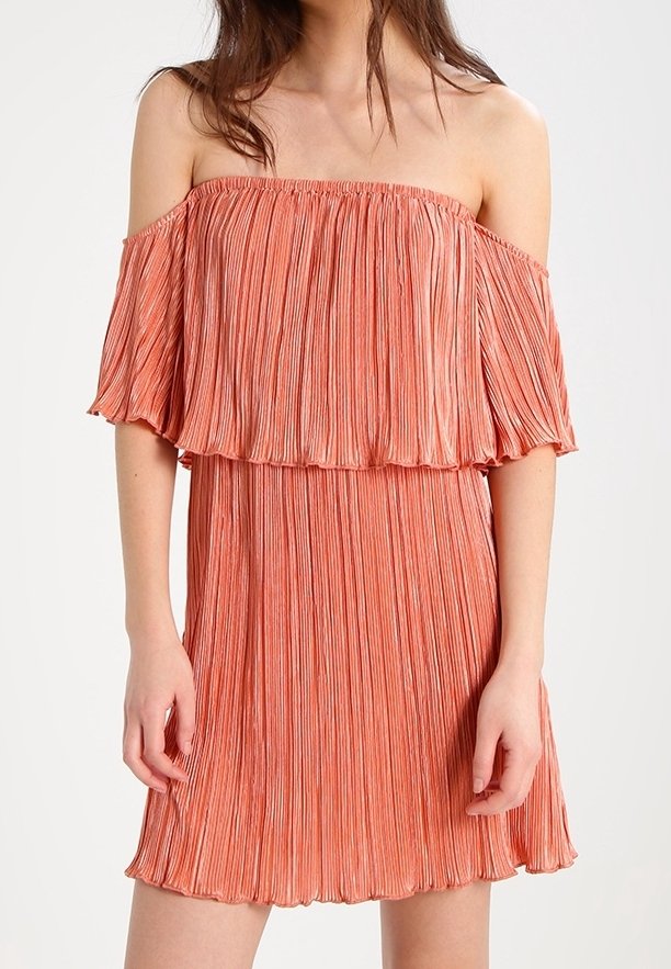 Robe plissée à épaules nues en corail, présentant un tissu texturé, une silhouette fluide et un ourlet évasé. Les manches courtes créent un effet superposé.