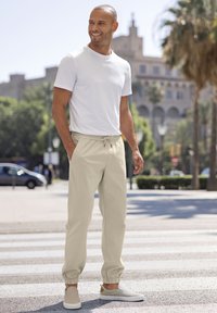 Lichte beige broek met trekkoord en elastische boorden, gecombineerd met een nauwsluitend wit T-shirt met korte mouwen en lichte instap schoenen.
