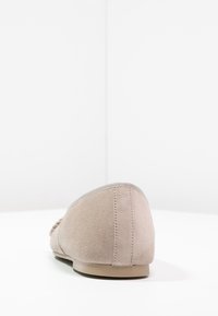 Beige ruskinds flad sko med en lav hæl, rund tå og quilted detaljer langs den øverste kant og hælen for tilføjet tekstur.